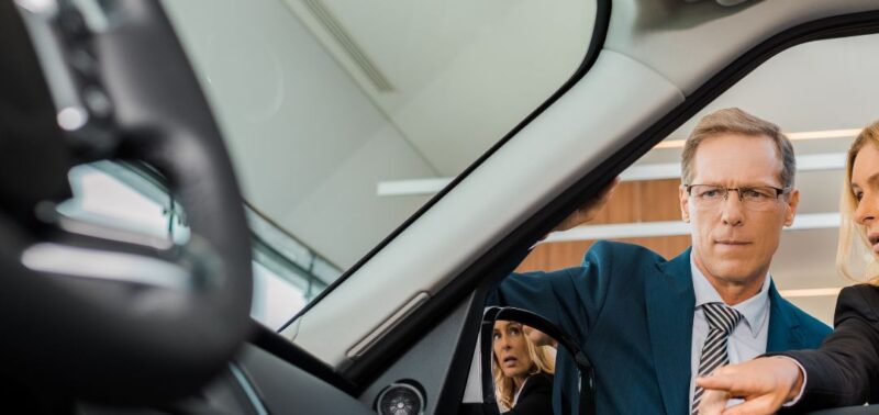 Zwei Personen in Businesskleidung begutachten gemeinsam das Innere eines Range Rover durch die geöffnete Fahrertür in einem modernen Autohaus. Der Fokus liegt auf dem Gespräch und dem hochwertigen Innenraum des Fahrzeugs.