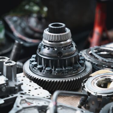 Nahaufnahme eines ausgebauten Getriebeteils mit präzise gefrästen Zahnrädern und mechanischen Komponenten. Das Teil liegt auf einer Werkbank, umgeben von weiteren Getriebebauteilen.